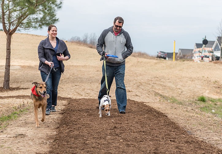 Couple walking dogs in Wendell Falls Dog Park